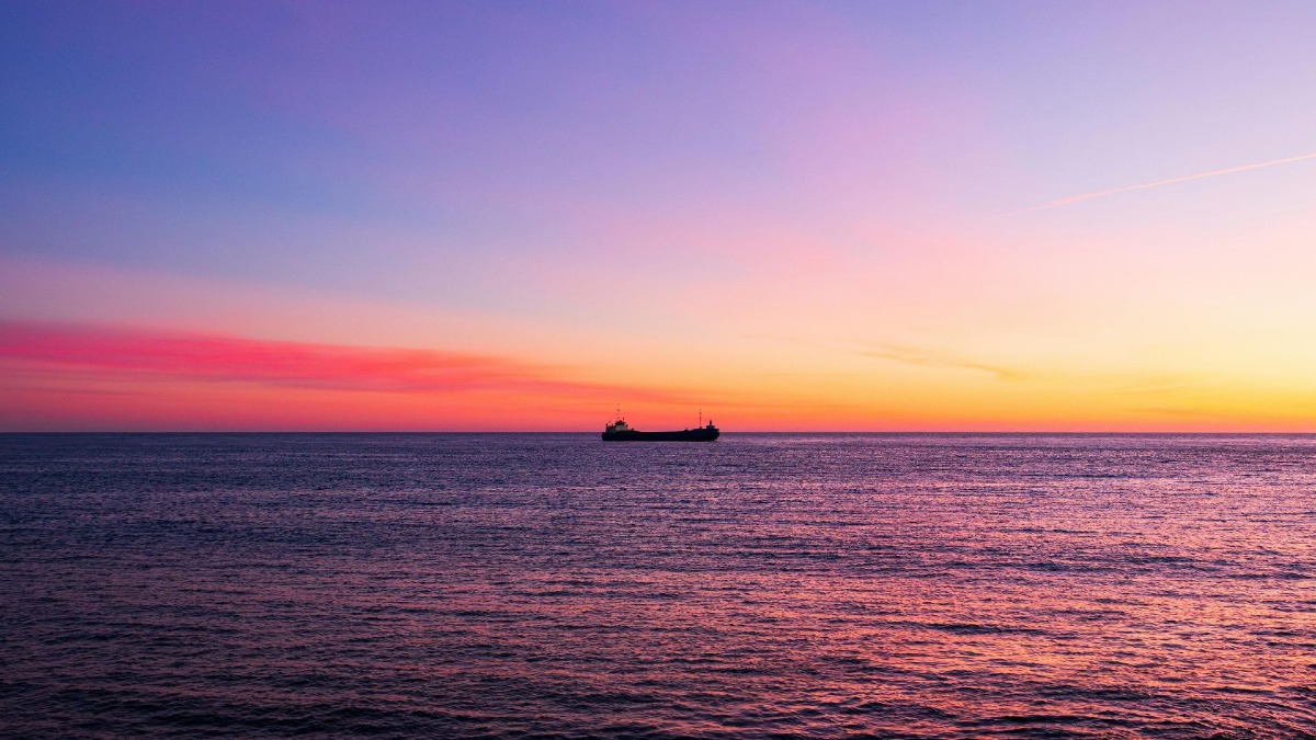 Magical sunset boat tour in Porto with a red and orange sky and a cargo ship in the distance